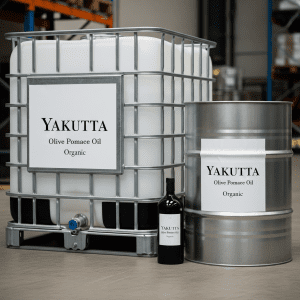 A close-up shot of an industrial IBC (Intermediate Bulk Container) and a metal drum, both featuring white labels that read "YAKUTTA Olive Pomace Oil Organic." A small dark bottle is partially visible between them. This image highlights industrial packaging for Yakutta Olive Pomace Oil.