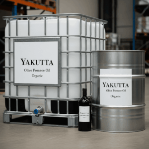 Gros plan sur un IBC (Intermediate Bulk Container) industriel et un fût métallique, tous deux munis d'étiquettes blanches indiquant "YAKUTTA Olive Pomace Oil Organic" (huile de grignons d'olive biologique). Une petite bouteille sombre est partiellement visible entre les deux. Cette image met en évidence l'emballage industriel de l'huile de grignons d'olive Yakutta.