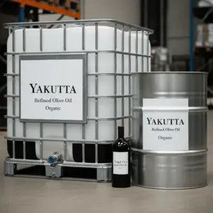 Primer plano de un contenedor industrial a granel (IBC) blanco y un bidón metálico, ambos claramente etiquetados como "YAKUTTA Aceite de Oliva Refinado Ecológico". Entre los dos contenedores más grandes se ve parcialmente una botella de vidrio oscuro. Esta imagen pone de relieve el envasado industrial del aceite de oliva refinado Yakutta.