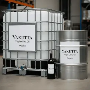 Un GRV industriel blanc et un fût métallique, tous deux munis d'étiquettes portant la mention "YAKUTTA Virgin Olive Oil Organic" (huile d'olive vierge biologique). Une bouteille en verre foncé est partiellement visible entre les deux. L'image met en évidence l'huile d'olive vierge biologique de la marque dans différents types d'emballage.
